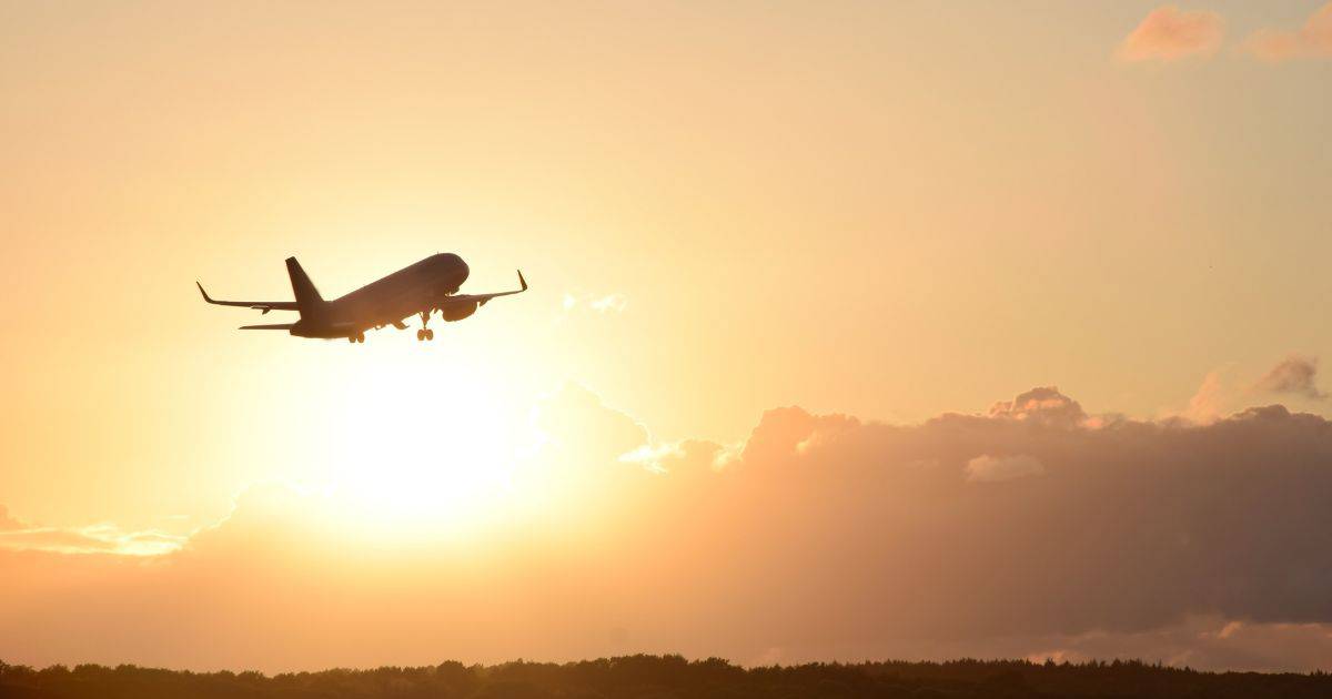 plane taking off on an airport runway with the sun in the distance