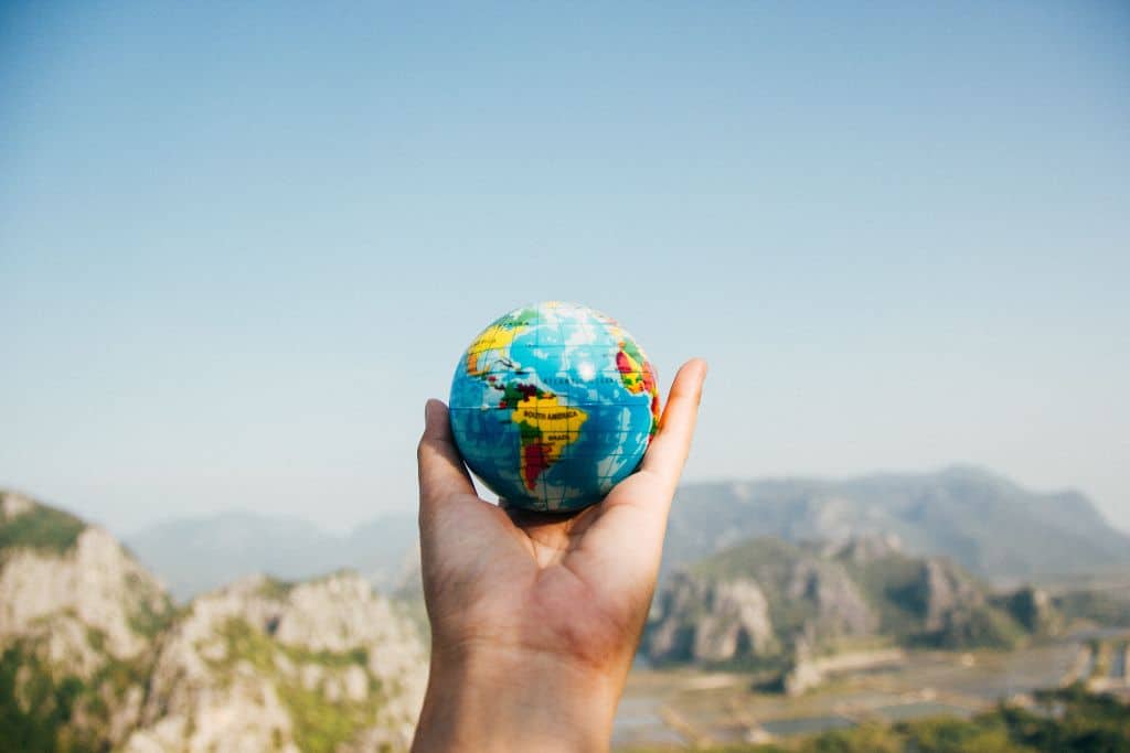 hand holding a world globe ball, with mountains in the background