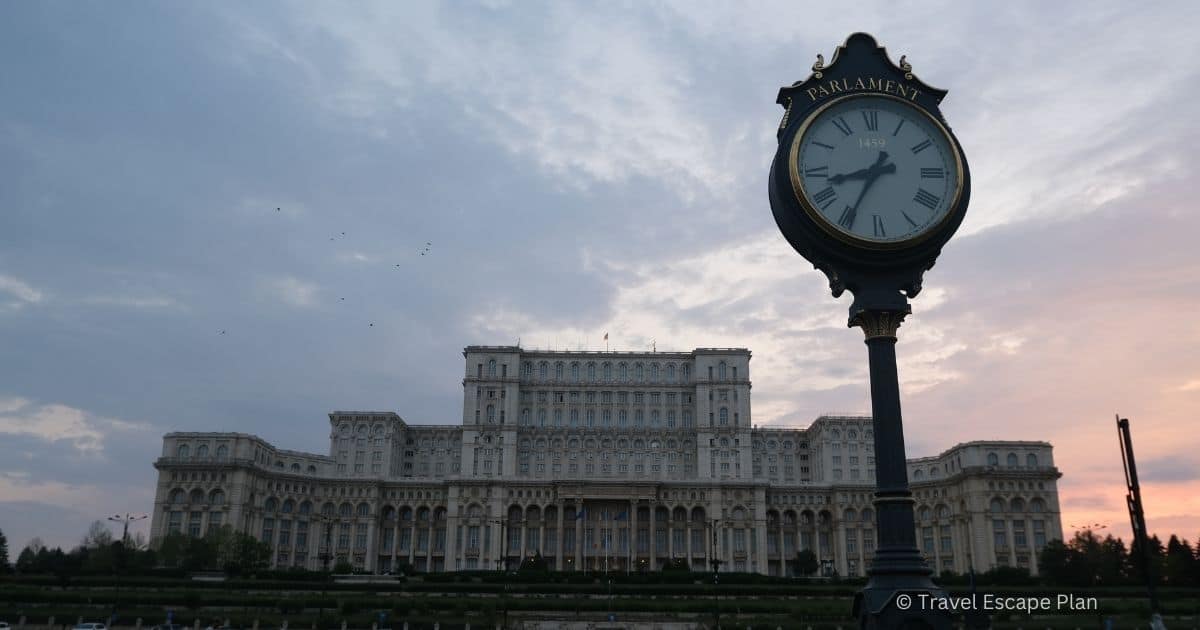 a clock in front the Palace of Parliament in Romania's Capital City at sunset