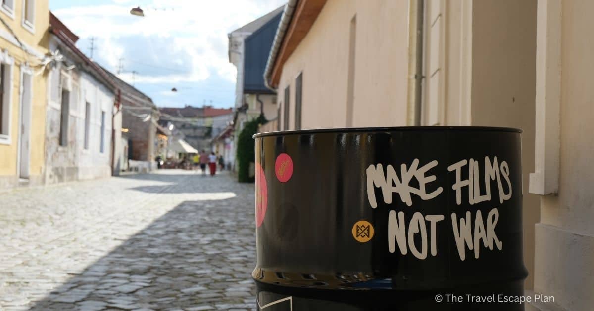 a close-up shot of a black metal barrel on a street in Cluj-Napoca, with graffiti that says "make films, not war" 