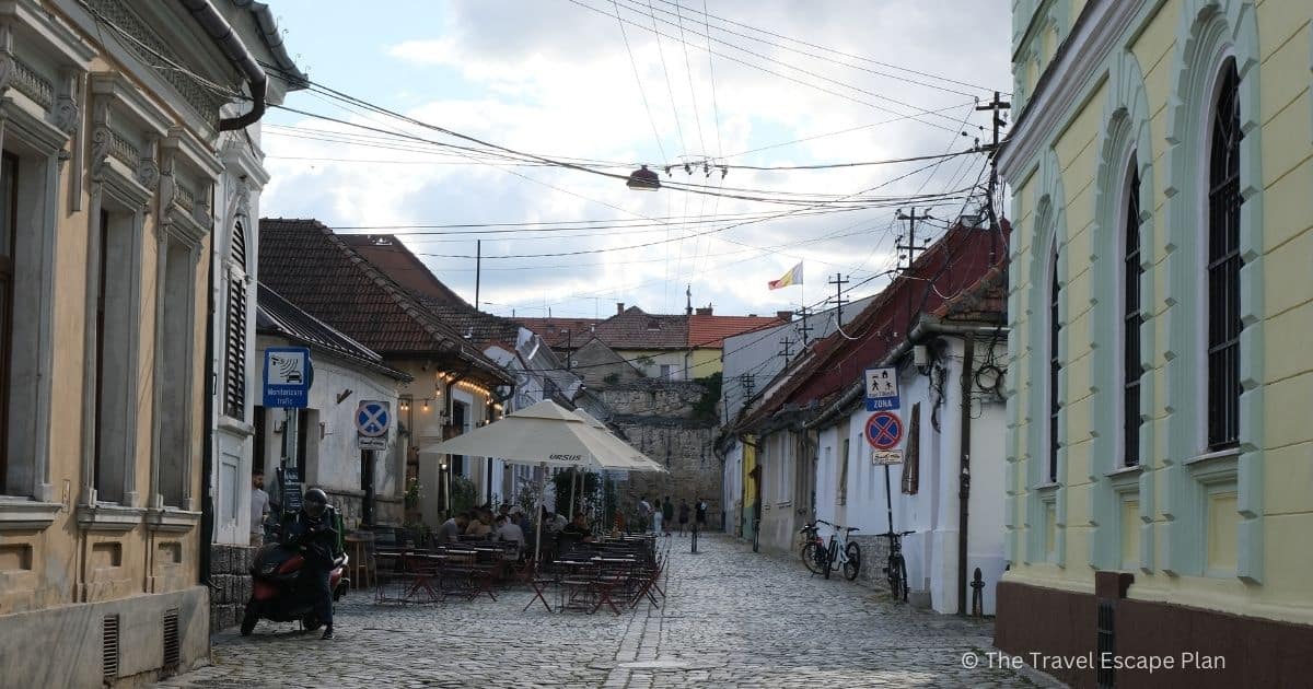 cobbled stone street in Cluj-Napoca Old Town with restaurant outdoor terraces and umbrellas