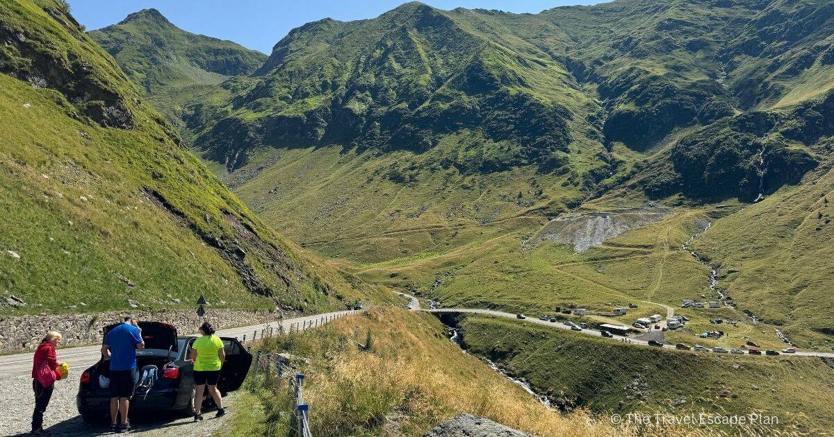 a family of 3 standing beside their car parked on the side of the Transfagarasan Highway with mountains in the background