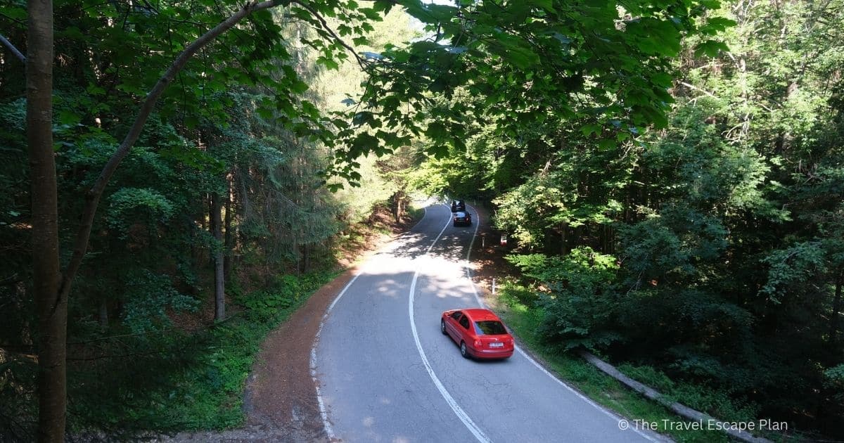 a red car driving past on the Transfagarasan Highway through the forest