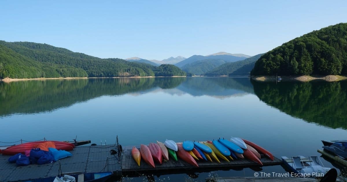 a stack of colourful kayaks on a wooden pontoon on Vidraru Lake, with mountain reflections in the water